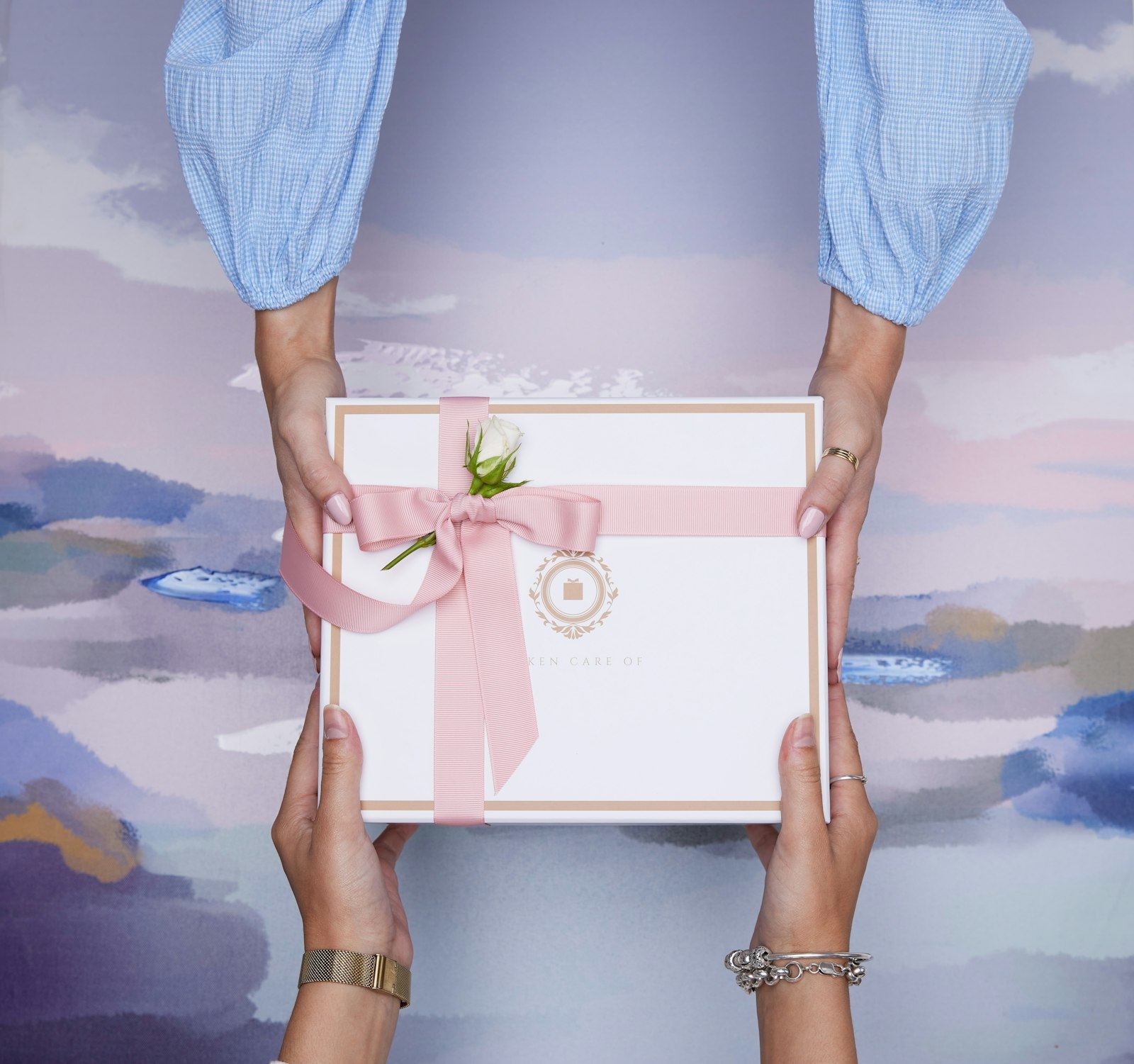 Two hands passing a wrapped gift box with a pink ribbon