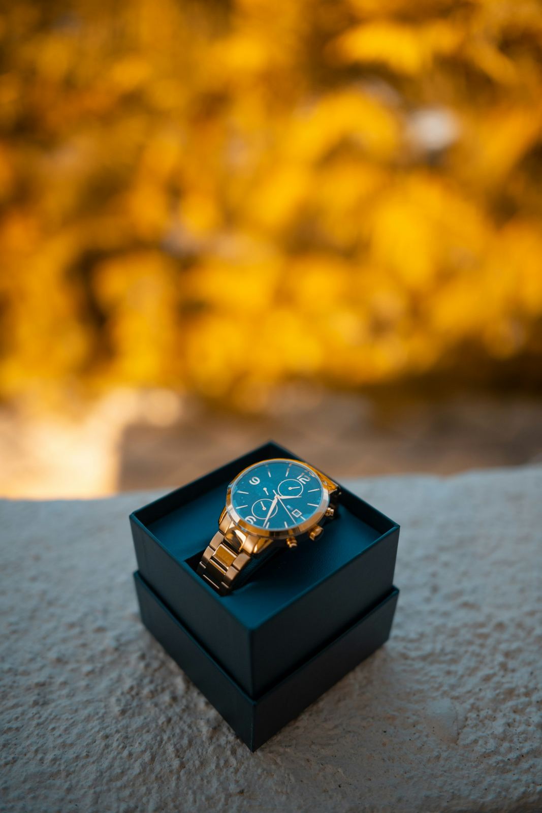 A gold watch with a teal dial resting in an open gift box